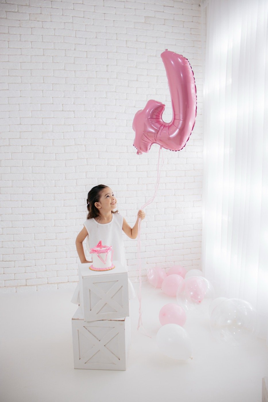 Menina sobre o cubo ao lado do balão com a inicial