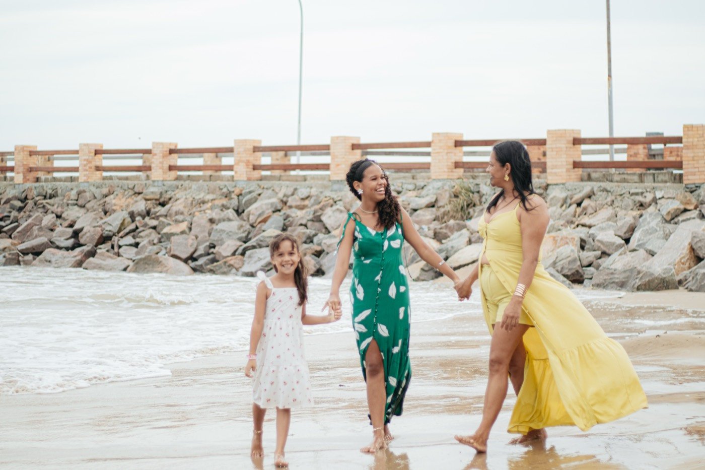 Mãe e filhas caminhando na beira da praia
